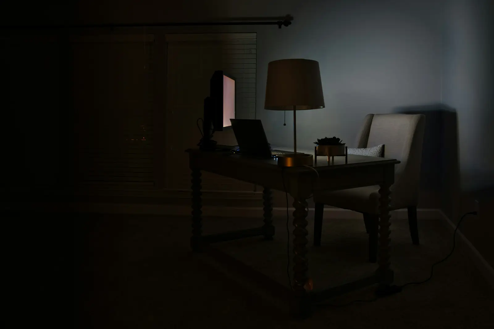 A dim study lit by a single table lamp, a laptop open on the desk