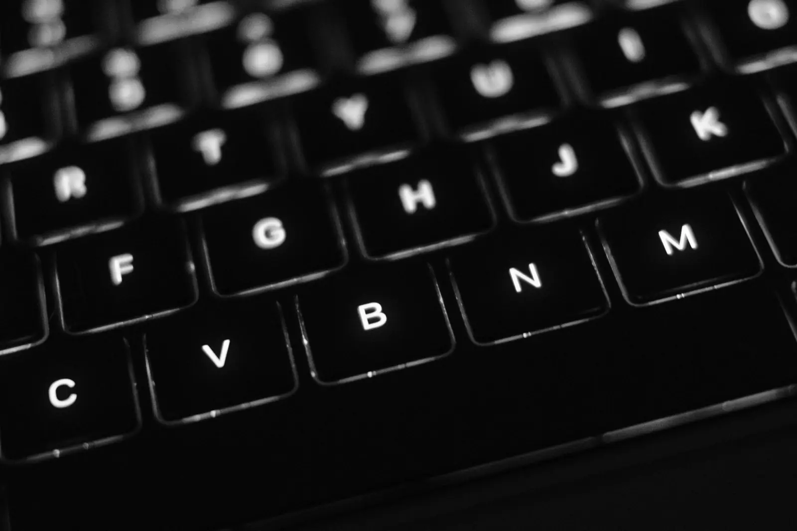 Close-up of a backlit laptop keyboard glowing in the dark